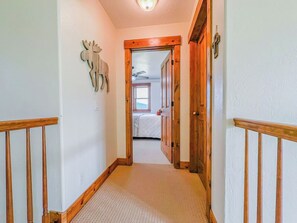 A hallway with wooden railings, a carpeted floor, and a door leading to a bedroom with a bed. - Foosball, Fireplace, Deck, Views, Guest Favorite (Alpine)