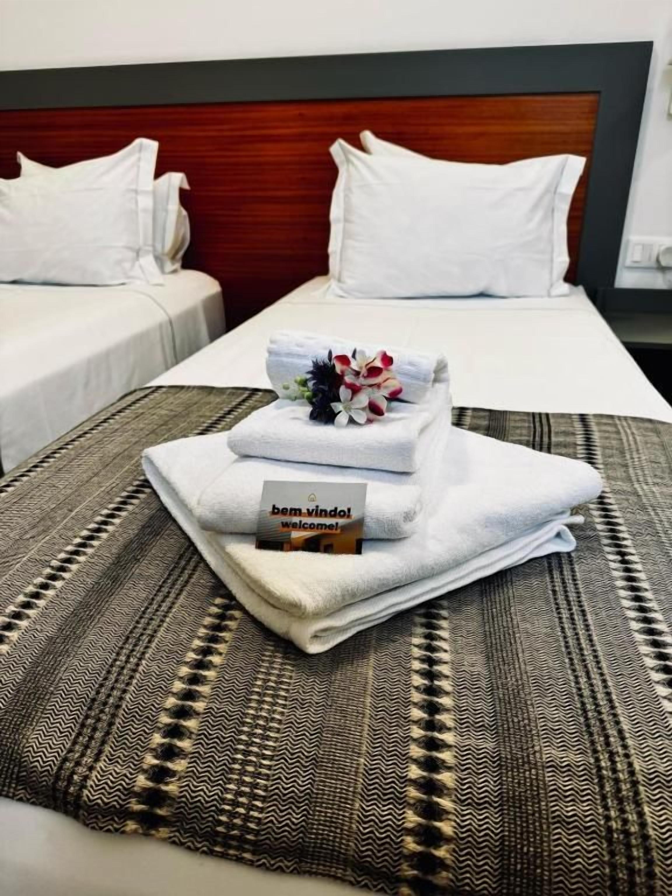 Hotellihuone, jossa on kaksi sänkyä, sängynpääty ja tervetulomatolla pyyhe sekä kortti.