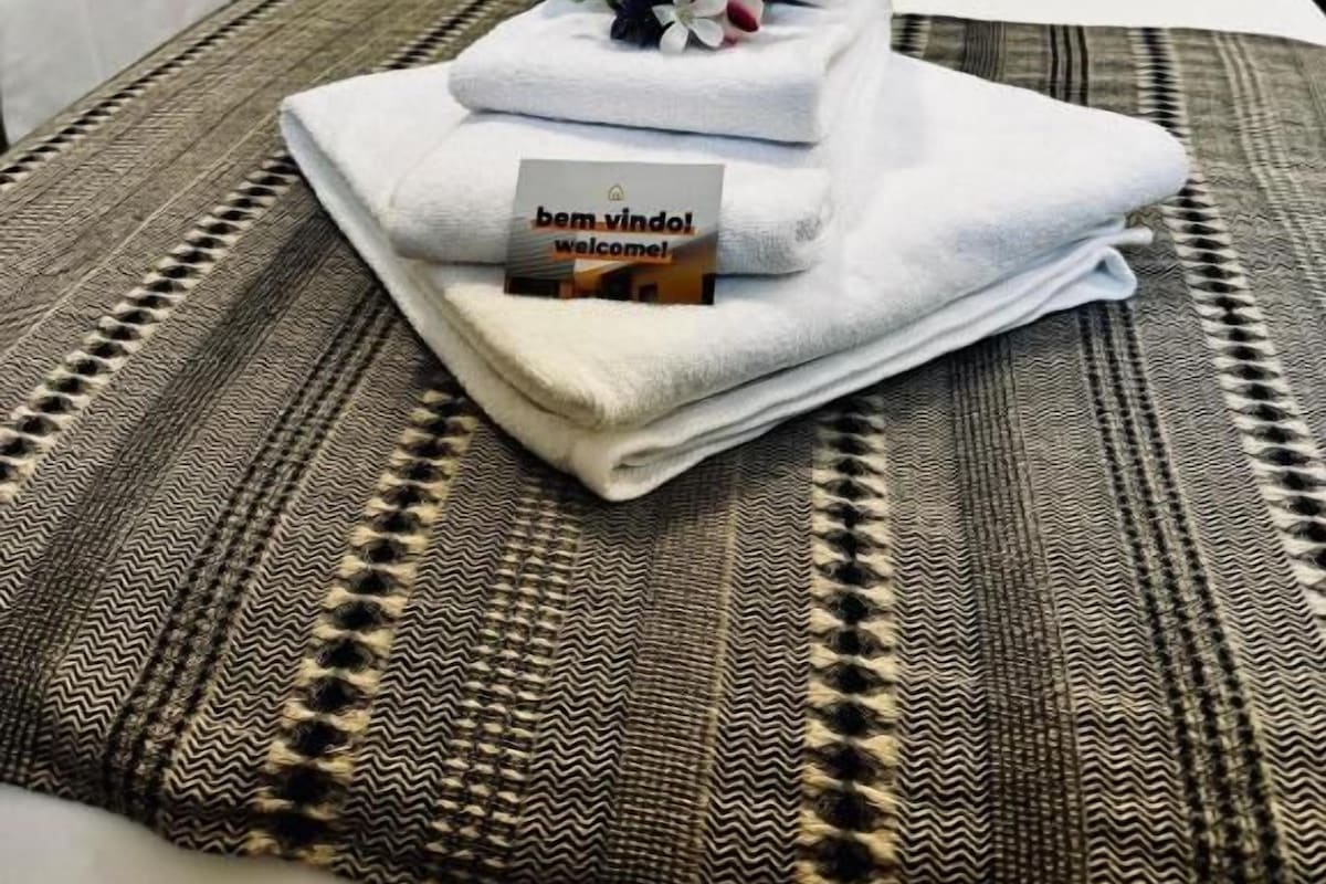 A hotel room with two beds, a headboard, and a welcome mat with a towel and a card.