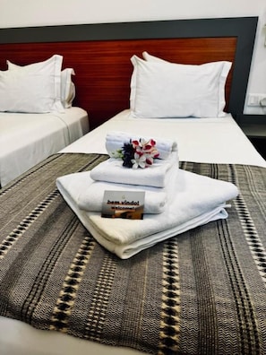 A hotel room with two beds, a headboard, and a welcome mat with a towel and a card. - Aliança Café & Hostel  (Angra do Heroísmo)