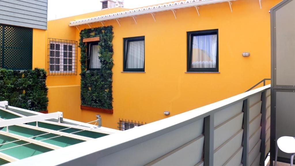 A yellow building with a balcony, a window with a curtain, and a metal railing.