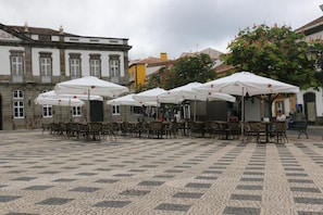 An outdoor café area with tables and chairs, umbrellas, and a cobblestone floor.
