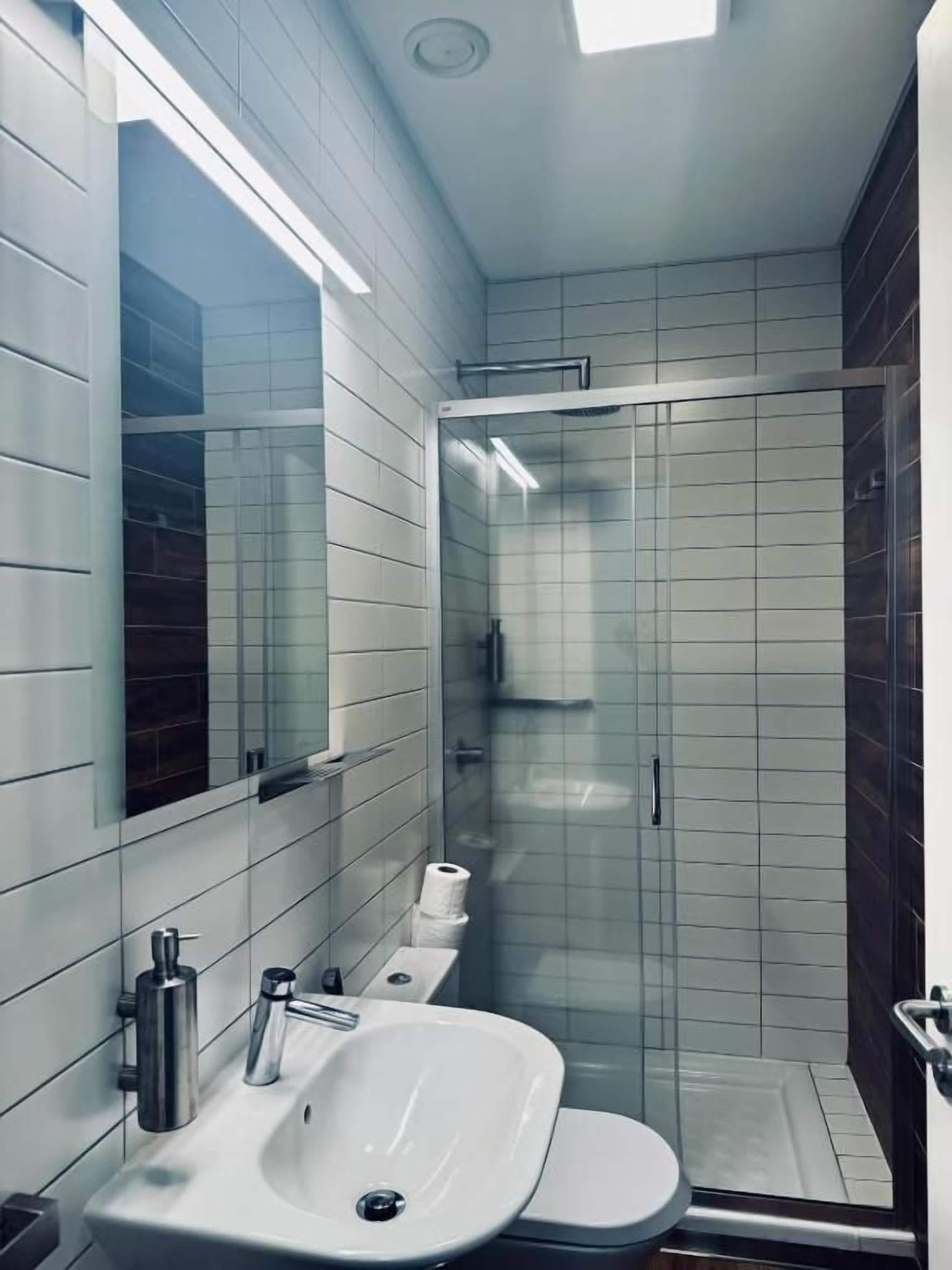 Casa de banho moderna com lavatório branco, sanita e cabine de duche com vidro.