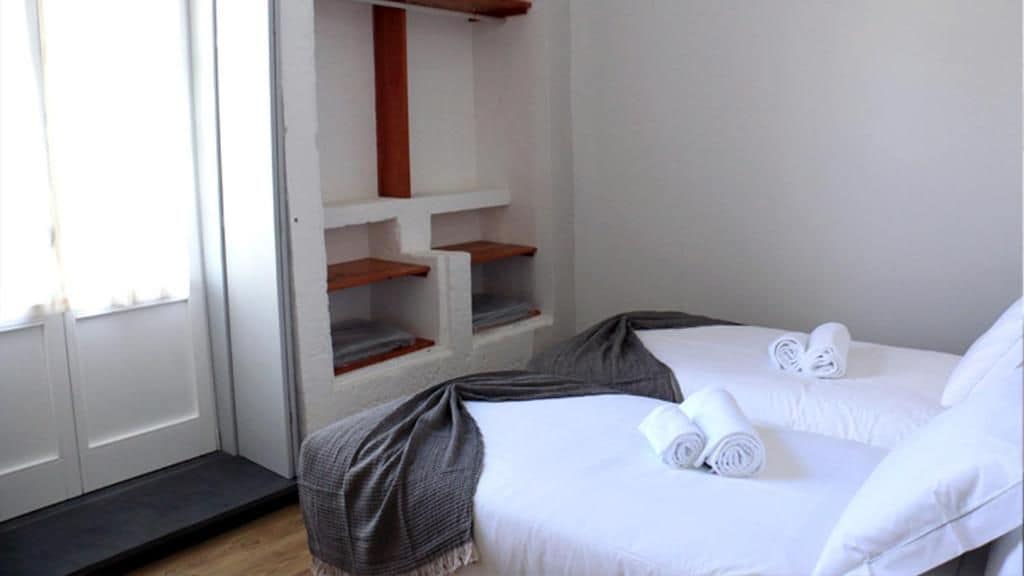 Une chambre d’hôtel avec deux lits, une étagère en bois et une porte donnant sur l’extérieur par un petit palier.
