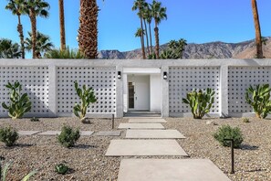 A pathway leading to a building with a perforated wall, surrounded by cacti and palm trees. - Indian Canyons Bauhaus Estate (Palm Springs)