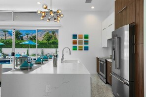 A modern kitchen with a central island, stainless steel appliances, and a view of a pool area. - Indian Canyons Bauhaus Estate (Palm Springs)