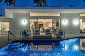 A modern building with a swimming pool, outdoor seating, and a well-lit interior. - Indian Canyons Bauhaus Estate (Palm Springs)