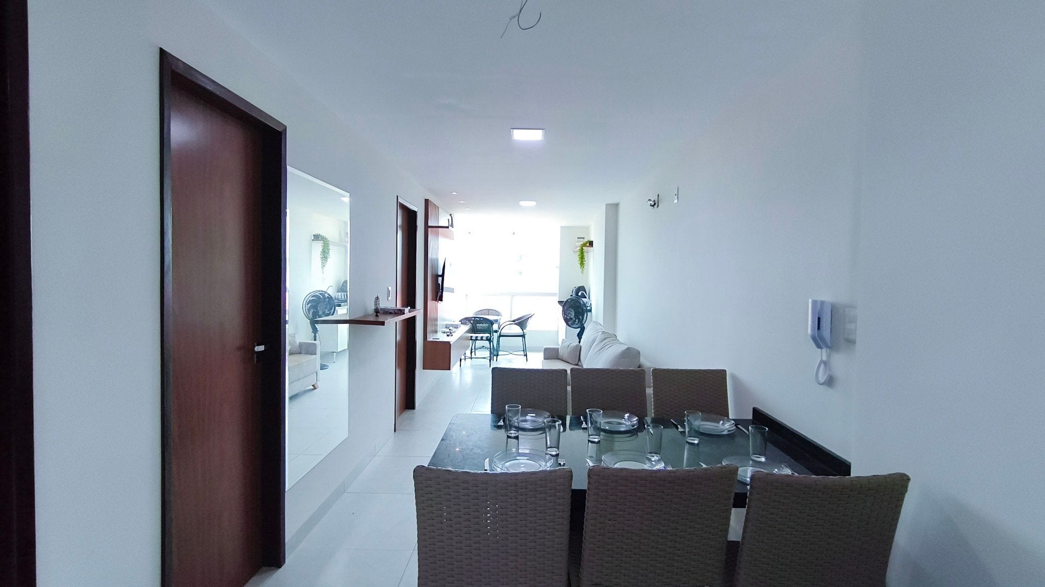Un'area pranzo moderna con un tavolo in vetro, sedie in vimini e vista sul soggiorno adiacente.