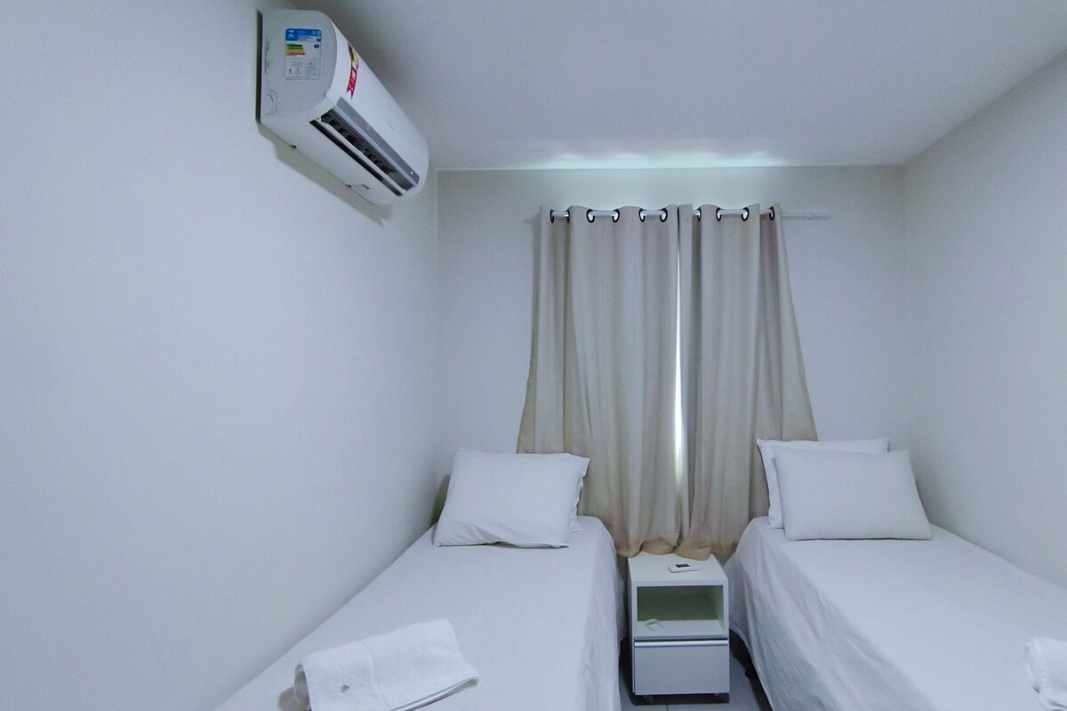 A single-bed room with a wall-mounted air conditioner, a bedside table with a phone, and a curtain.