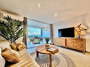 A modern living room with a sofa, coffee table, and a TV on a wooden cabinet. - BlueDream Studio - Panoramic View, Pool, and Beach (Saint Martin)