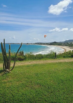 A coastal landscape with a grassy foreground, a beach, and a clear sky. - BlueDream Studio - Panoramic View, Pool, and Beach (Saint Martin)