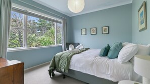 A bedroom with a bed, a bedside table, a window with curtains, and framed pictures on the wall.