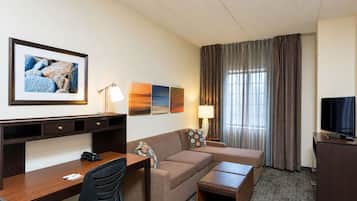 A hotel room with a desk, a sofa, a TV, and a window with curtains.