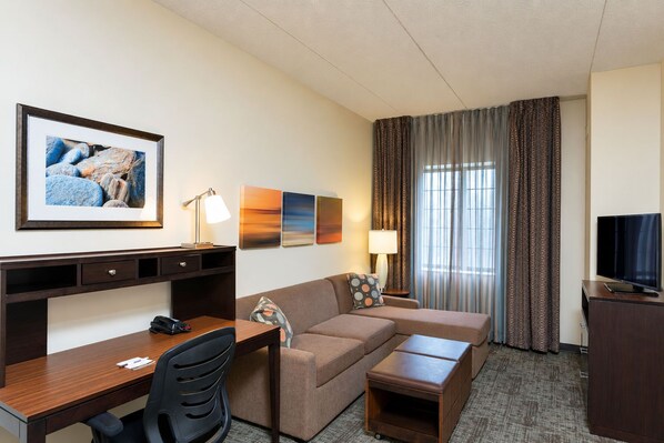 A hotel room with a desk, a sofa, a TV, and a window with curtains.