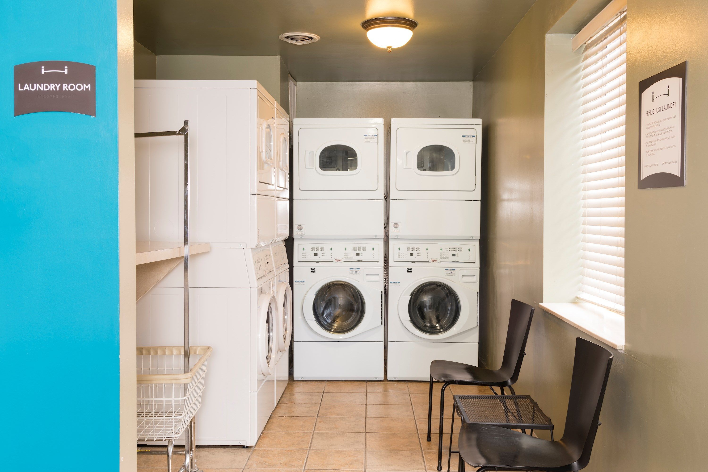 A laundry room with stacked washers and dryers, a white basket, and a table with chairs.