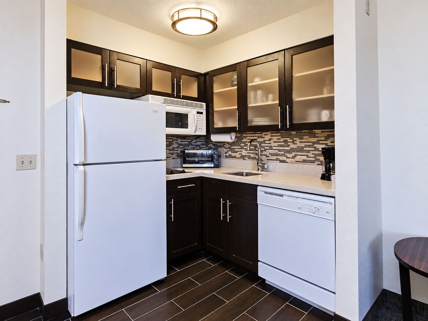 A compact kitchen with a refrigerator, microwave, toaster, sink, and dishwasher.