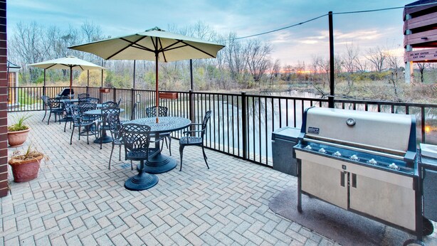 Un patio al aire libre con una parrilla, mesas, sillas y sombrillas.