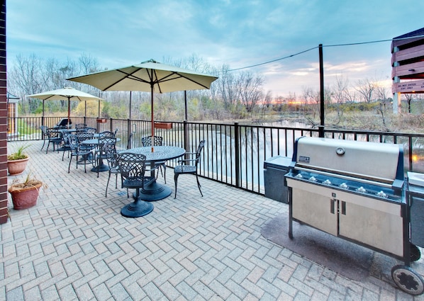 An outdoor patio with a grill, tables, chairs, and umbrellas. - Accessible 1BR Suite w/ Kitchen & Hot Breakfast (Oakbrook Terrace)