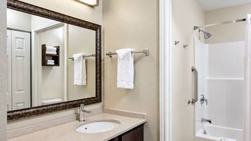 A bathroom with a sink, mirror, towel rack, and a shower area.