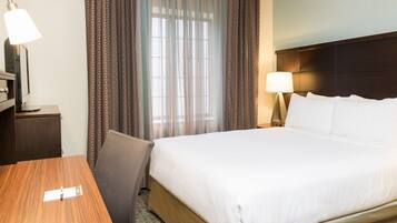 A hotel room with a bed, a desk, a chair, a lamp, and curtains.