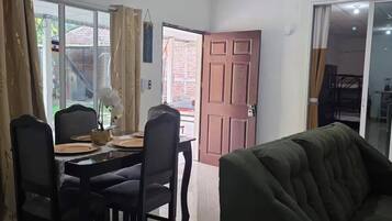 Et spiseområde med et bord, stole og en sofa. En skydedør fører ud til et udendørs område.