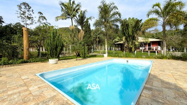 A rectangular swimming pool with a clear blue water surface, surrounded by a paved area with a mix of stone and concrete tiles. - ASA Esmeralda Refuge Lounge Pool Itajai (Itajai)