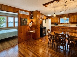 Un interior de madera con una mesa de comedor, sillas, estufa y un banco junto a una ventana.