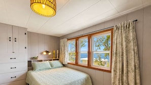 Een slaapkamer met een bed, een kledingkast, een raam met gordijnen en een hanglamp.