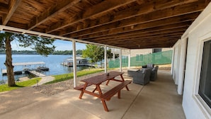 Een overdekt terras met een houten bank en tuinmeubilair, met uitzicht op een waterpartij en een steiger.