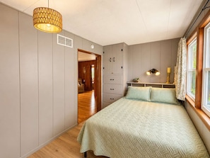 Un dormitorio con cama, armario, una puerta que da a otra habitación y ventana con cortinas.