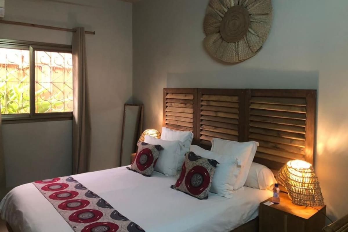 Een slaapkamer met een bed, kussens, een decoratief object aan de muur en een bedlampje.
