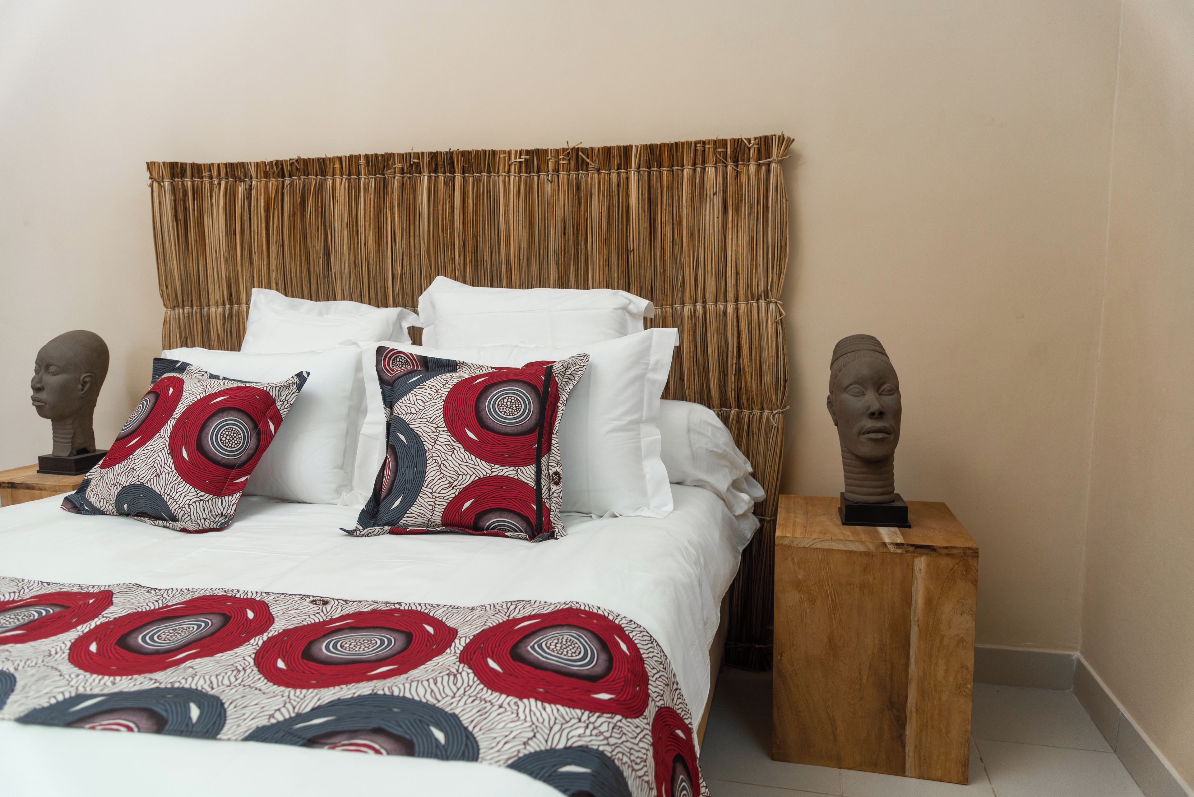 Een bed met witte beddengoed, gestreepte kussens en twee houten nachtkastjes met bustes.