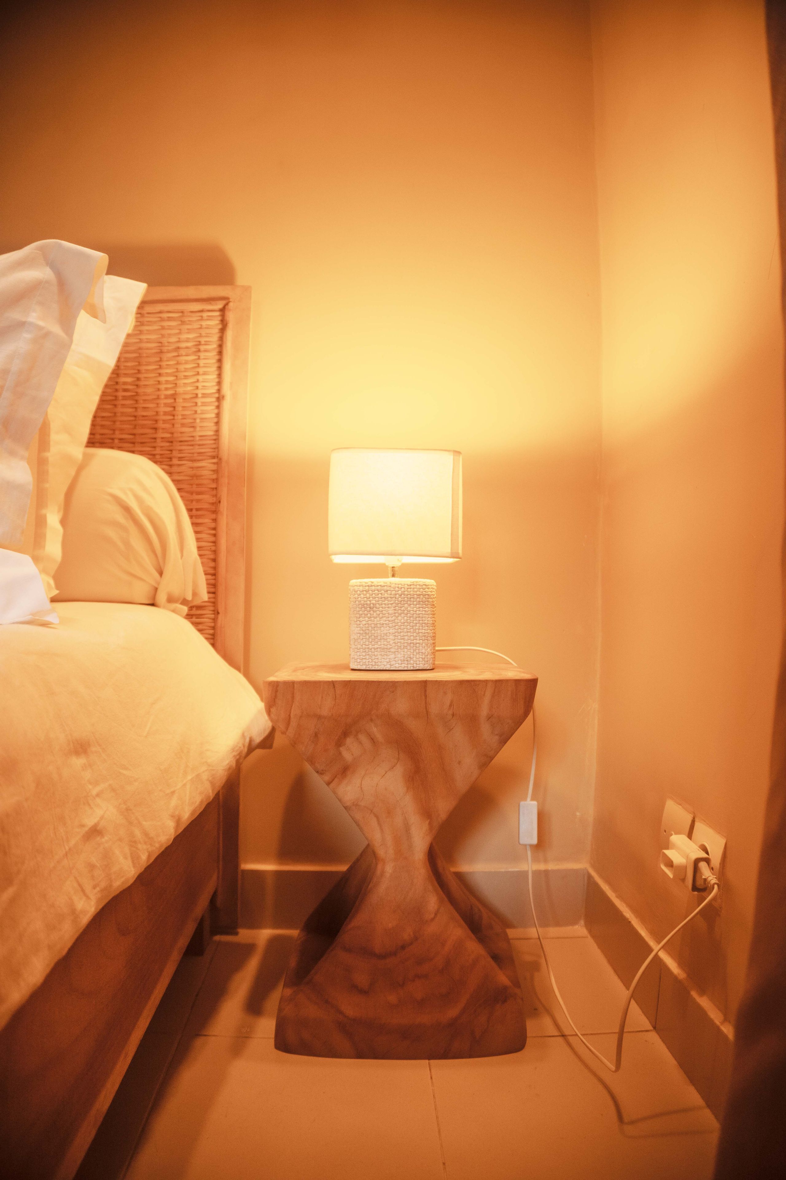 Una habitación de hotel con una cama, una mesita de noche con lámpara y un enchufe.