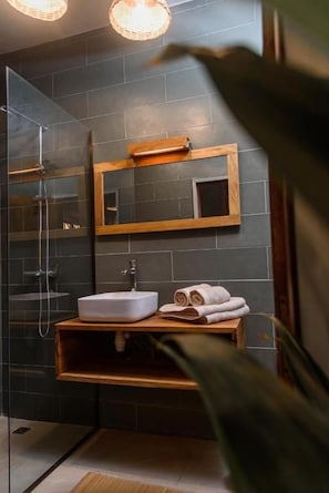 Een badkamer met een douchecabine van glas, een witte wastafel en een houten opbergmeubel.