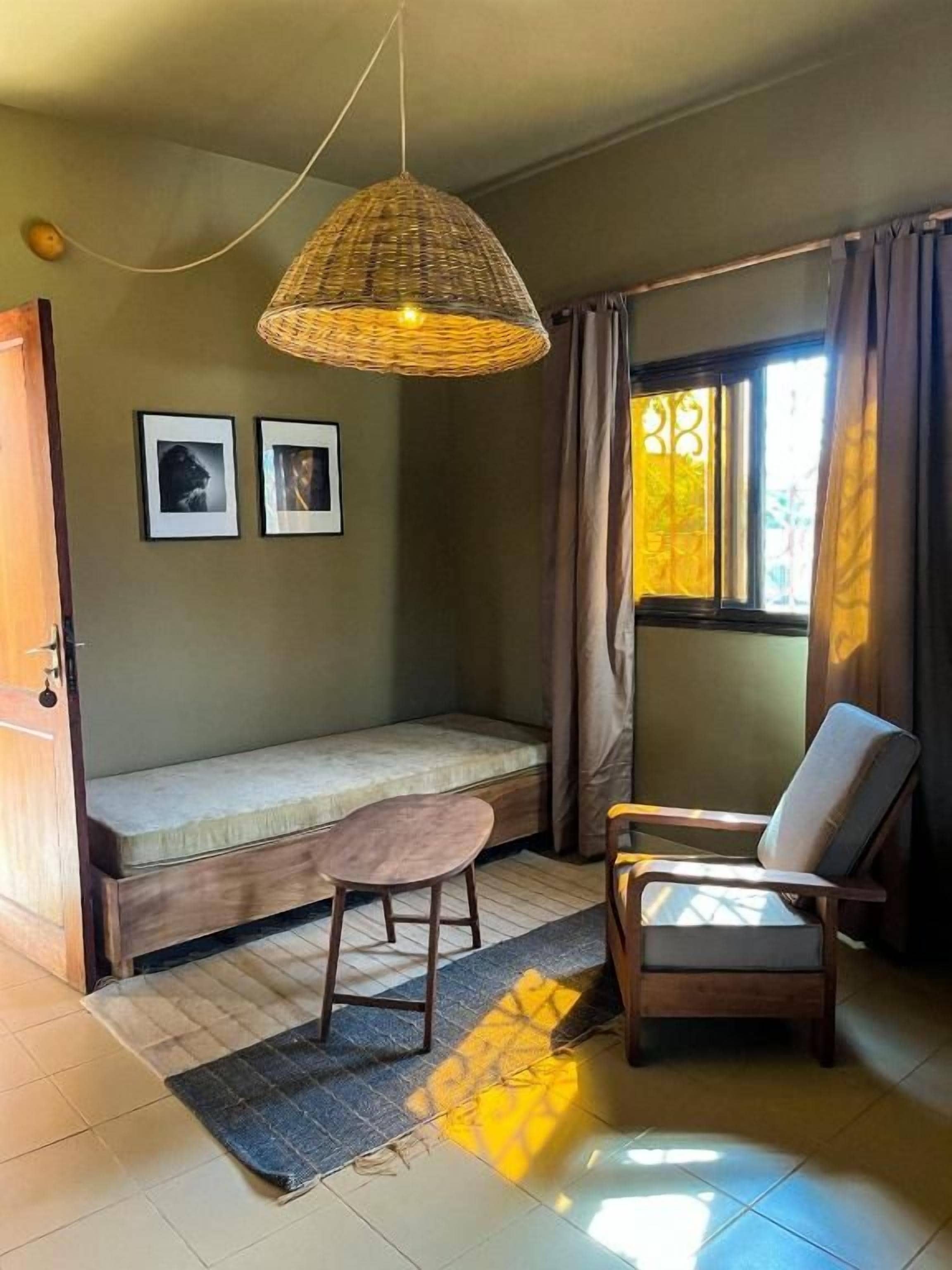 A room with a bed, a chair, a hanging light fixture, and a window with curtains.
