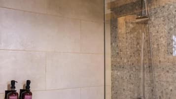 A shower area with a glass partition, a handheld showerhead, and two bottles of shampoo.