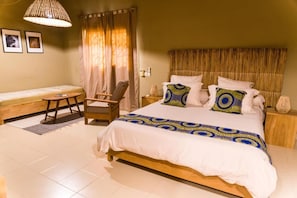 Een slaapkamer met een bed, een stoel, een klein tafeltje en gordijnen.