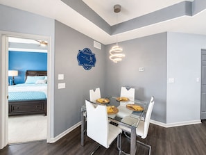 A modern hotel room with a glass dining table, white chairs, a blue accent wall, and a ceiling light fixture. - Emerald Escape Lake Views (Lake Ozark)