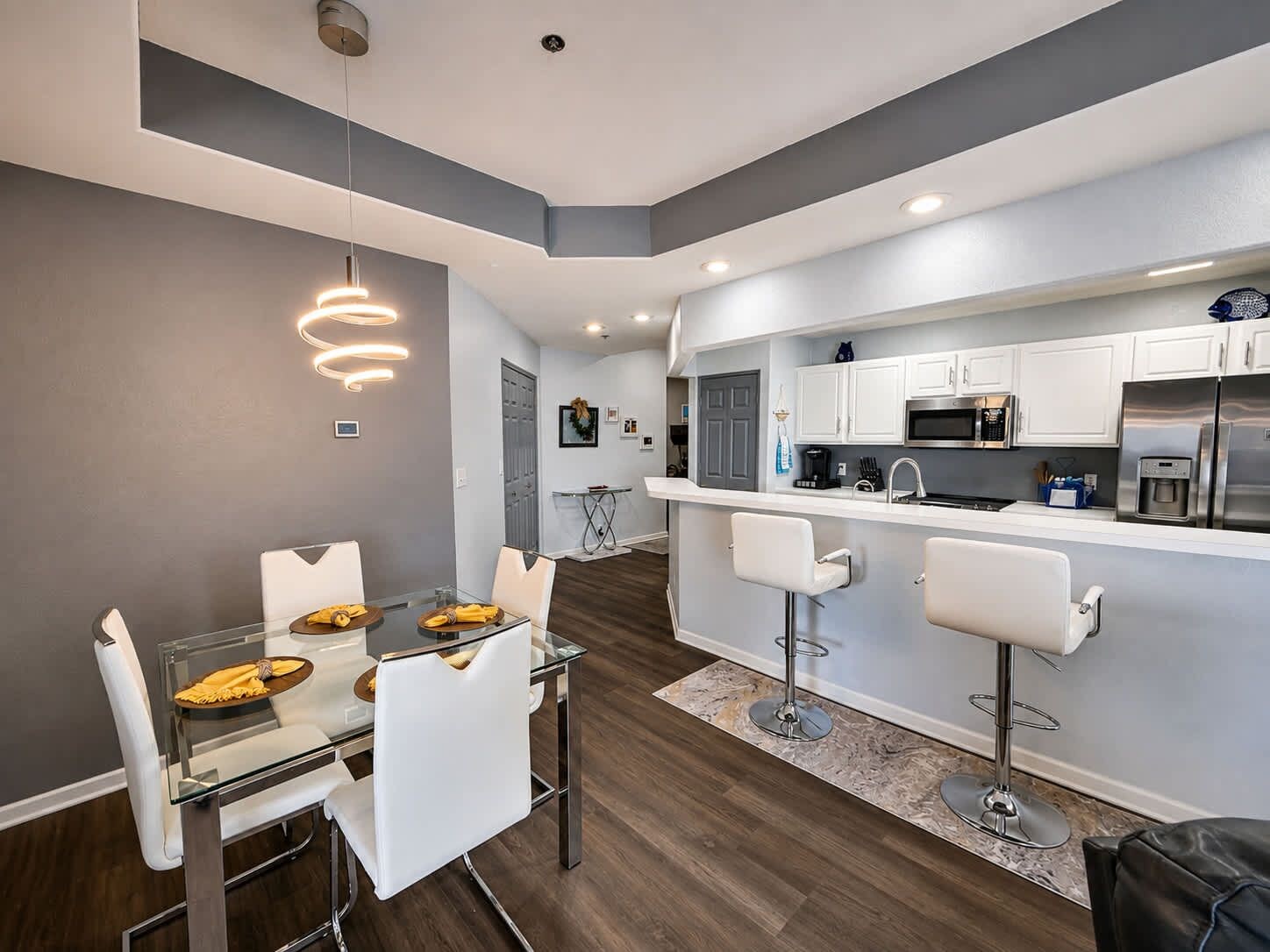A modern kitchen with white cabinets, stainless steel appliances, and a bar area with white bar stools.