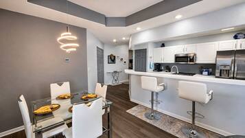 A modern kitchen with white cabinets, stainless steel appliances, and a bar area with white bar stools.