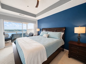 A bedroom with a large bed, a nightstand, a lamp, and a view of a body of water through a sliding door. - Emerald Escape Lake Views (Lake Ozark)