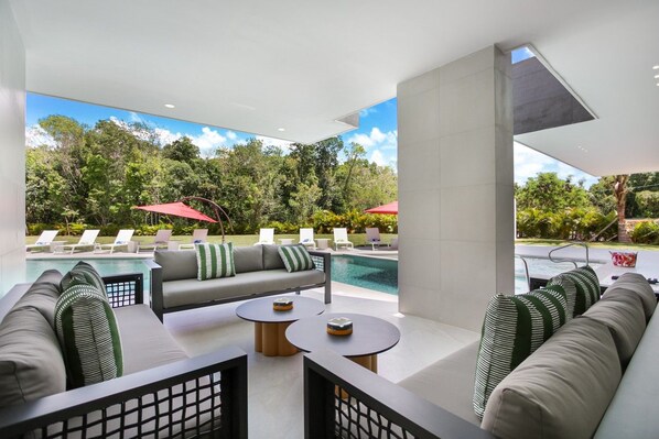 Ein moderner Außen-Loungebereich mit Pool, Sitzgelegenheiten und Blick auf die grüne Umgebung.