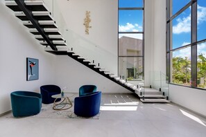 Ein modernes Interieur mit einer Glasstiege, blauen Stühlen und Blick ins Grüne.