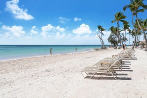 Ein Strand mit weißem Sand, Palmen und einer Reihe leerer Liegen.