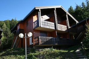A wooden cabin with a balcony, a staircase, and a small garden area. - 100m from ski slopes, Ground floor, balcony, parking, tv, ski locker, 30m², La Norma (La Norma)