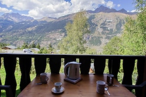 A wooden table with a kettle, cups, and saucers on a balcony overlooking a mountainous landscape. - 100m from ski slopes, Ground floor, balcony, parking, tv, ski locker, 30m², La Norma (La Norma)