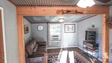 Une pièce avec un plafond en bois, un ventilateur de plafond, une horloge, un canapé, un téléviseur et un tapis à motifs.