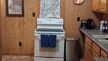 A kitchen with wooden cabinets, a white stove, a trash can, and a coffee machine.