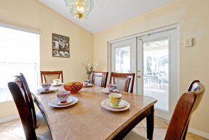 A dining room with a table set for four, chairs, a chandelier, a door with a view, and a framed picture on the wall. - Oakhill - Fairytale Villa 10 Mins From Disney (Kissimmee)