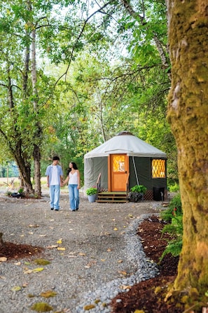 A couple walking towards a tented accommodation surrounded by trees. - New Leaf Greenhouse (Cornelius)